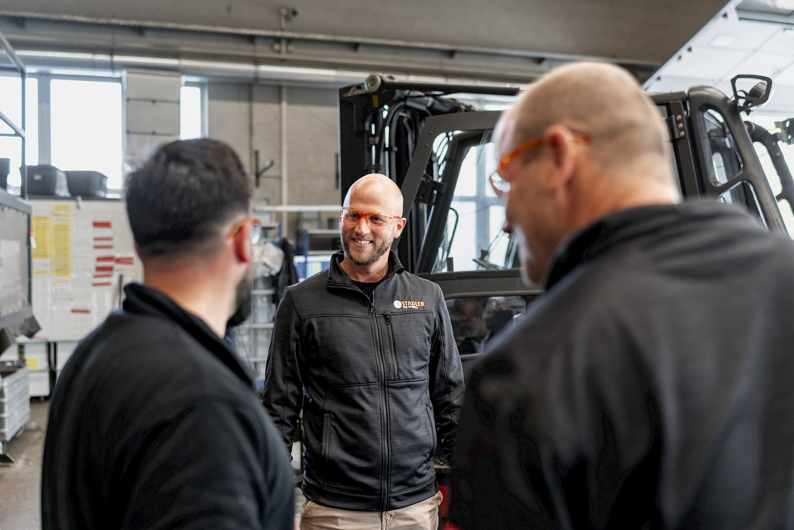 Drei Männer im Gespräch in einer Werkstatt.