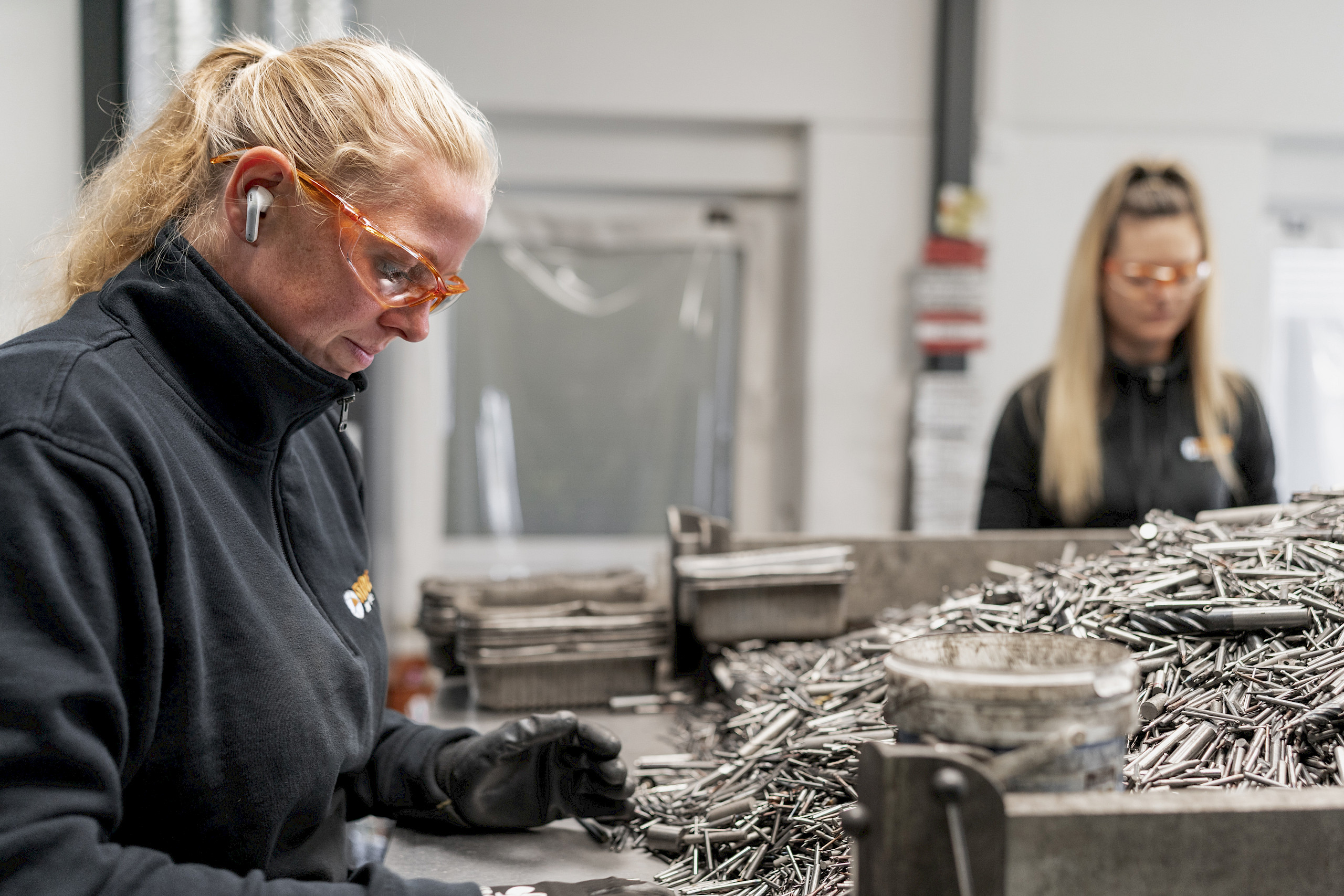 Zwei Frauen sortieren Metallteile in einer Werkstatt.